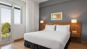 A hotel room with a large bed, two bedside lamps, a window with curtains, and a painting on the wall.
