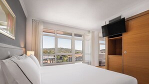 Habitación de hotel con una cama grande, un televisor montado en la pared y una ventana con vistas a la ciudad.