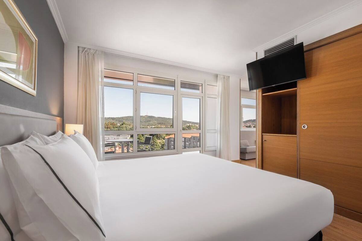 A hotel room with a large bed, a TV mounted on the wall, and a window with a city view.