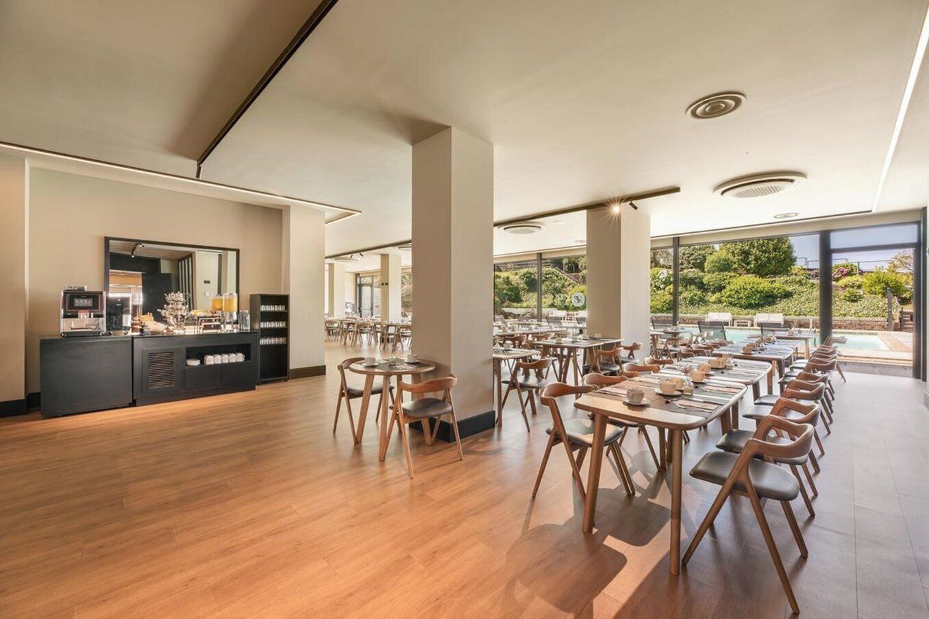 A spacious dining area with wooden tables and chairs, a buffet counter, and large windows offering a view of the outdoors.