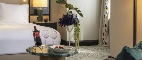 A hotel room with a bed, a seating area with a table, a vase with flowers, and a lamp.