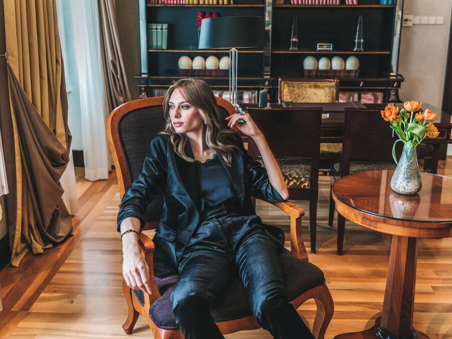 Una persona sentada en una silla en una habitación con piso de madera, una mesa redonda de vidrio con un florero y una estantería al fondo.