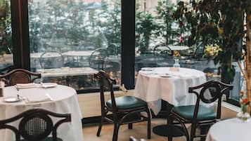 A restaurant with round tables and chairs, large windows, and a view of the street.