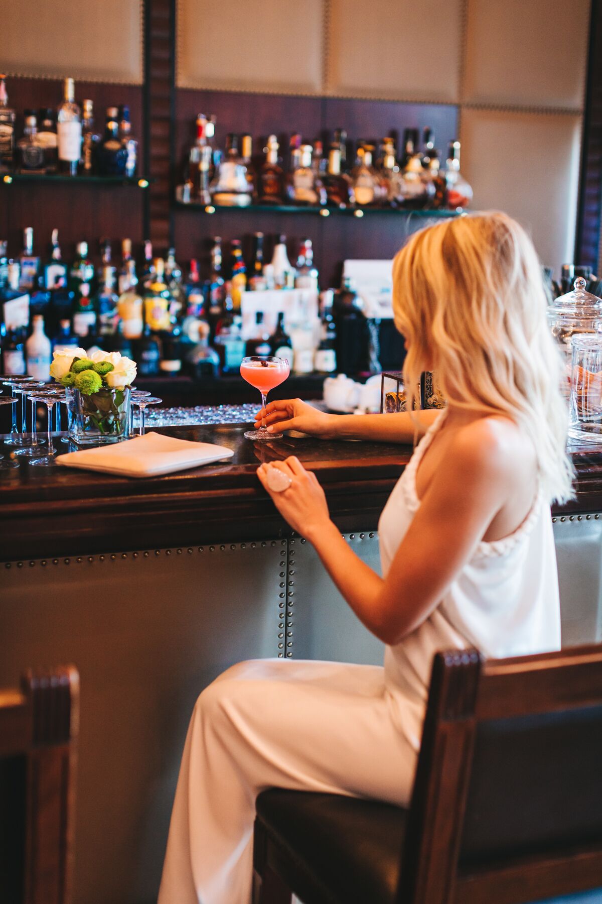A person seated at a bar with a variety of bottles and glasses in the background.