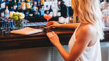 Una persona sentada en la barra, con una variedad de botellas y vasos al fondo.