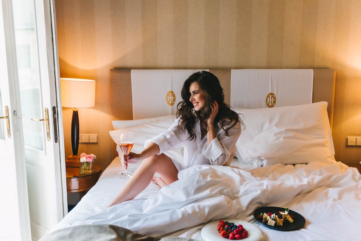 A hotel room with a bed, a bedside table with a lamp, and a plate of fruit.