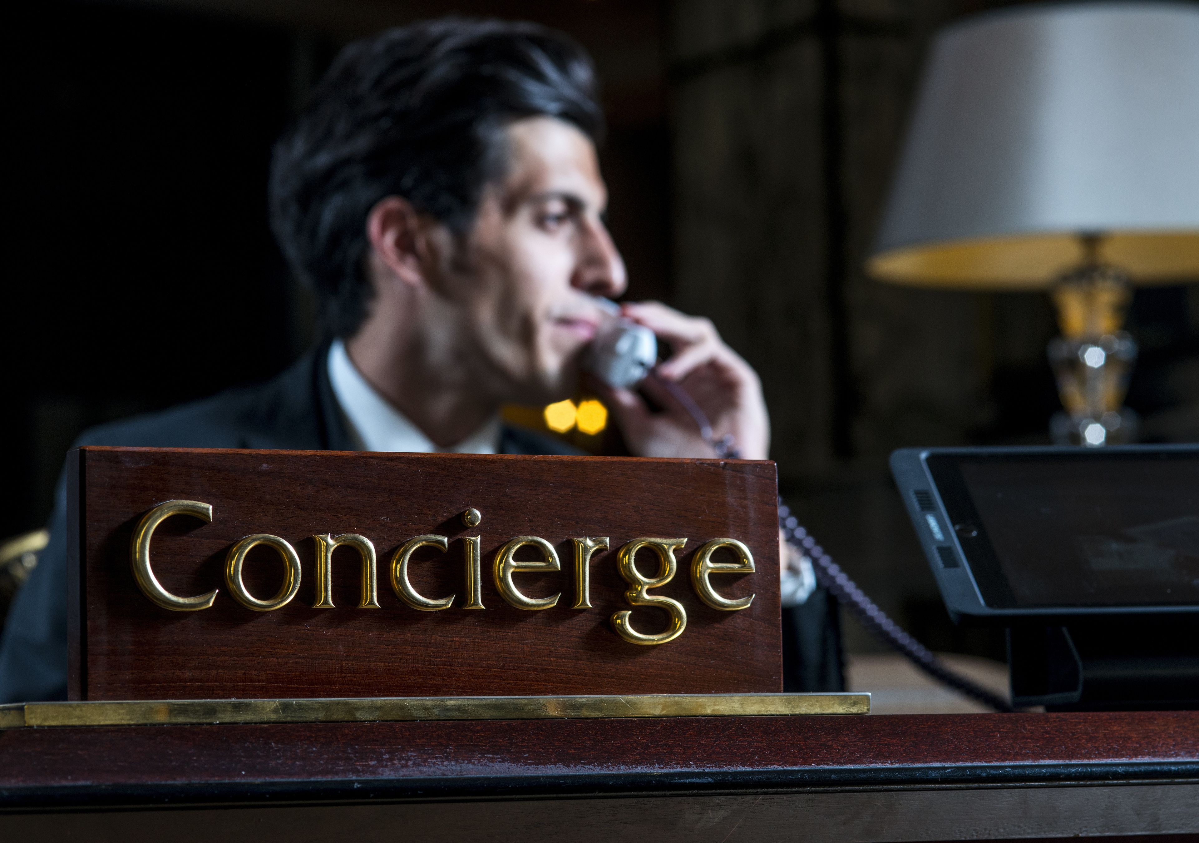 A concierge desk with a sign that reads "Concierge" and a lamp in the background.