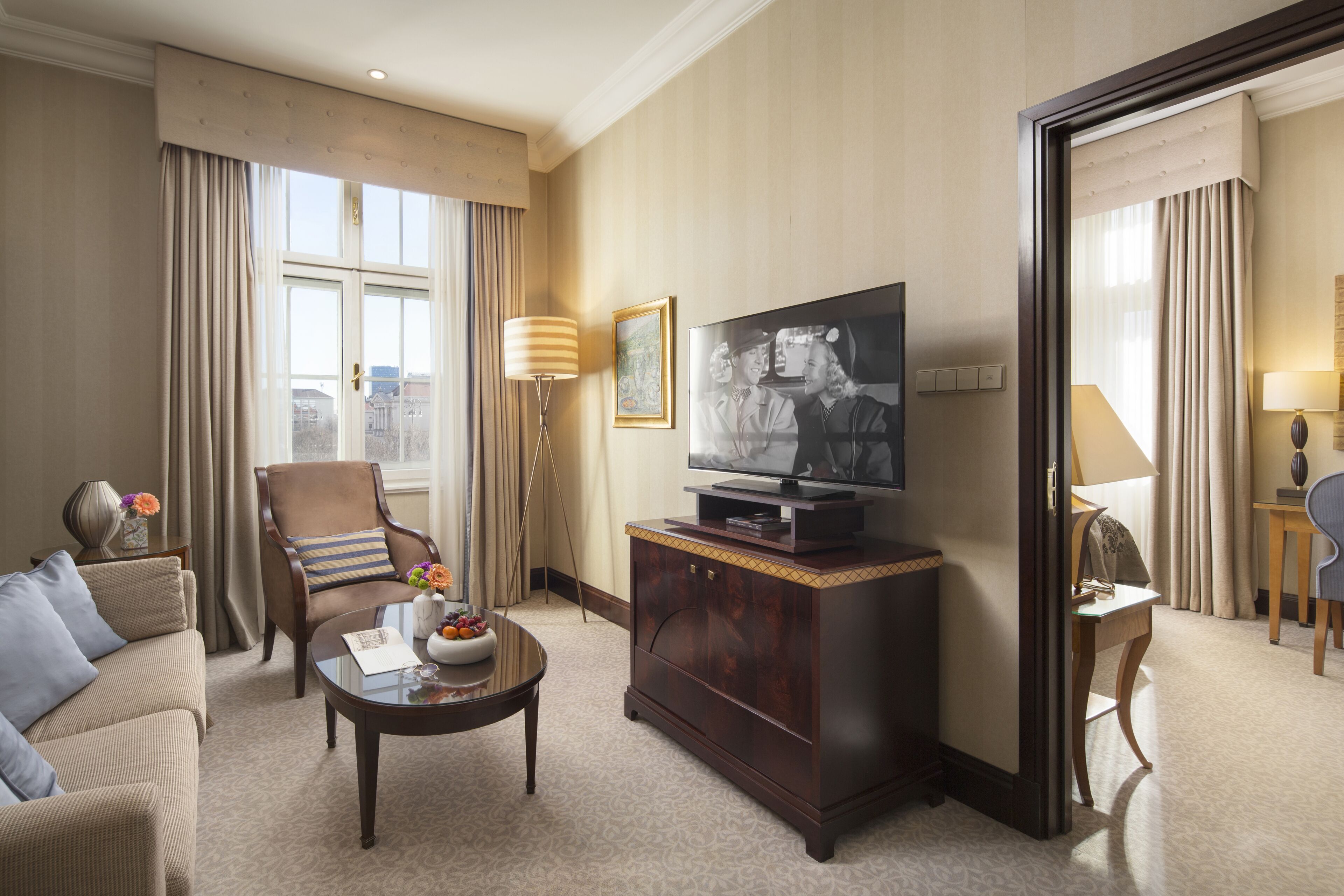 A hotel room with a sofa, armchair, coffee table, television, and a mirror.