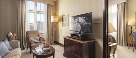 Habitación de hotel con sofá, sillón, mesa de centro, televisión y espejo.