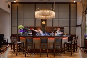 A bar area with a large chandelier, wooden bar counter, and multiple bar stools.