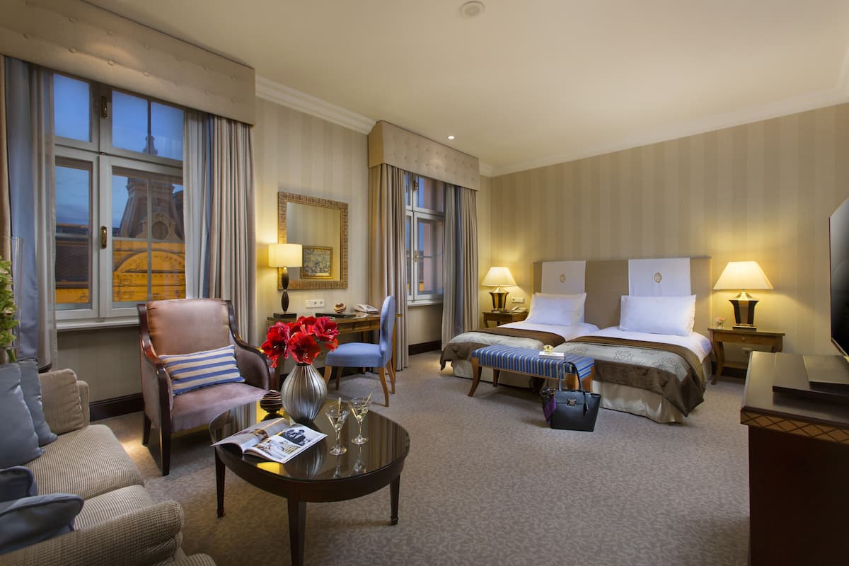 A hotel room with a sofa, armchair, two beds, a desk, and a TV.