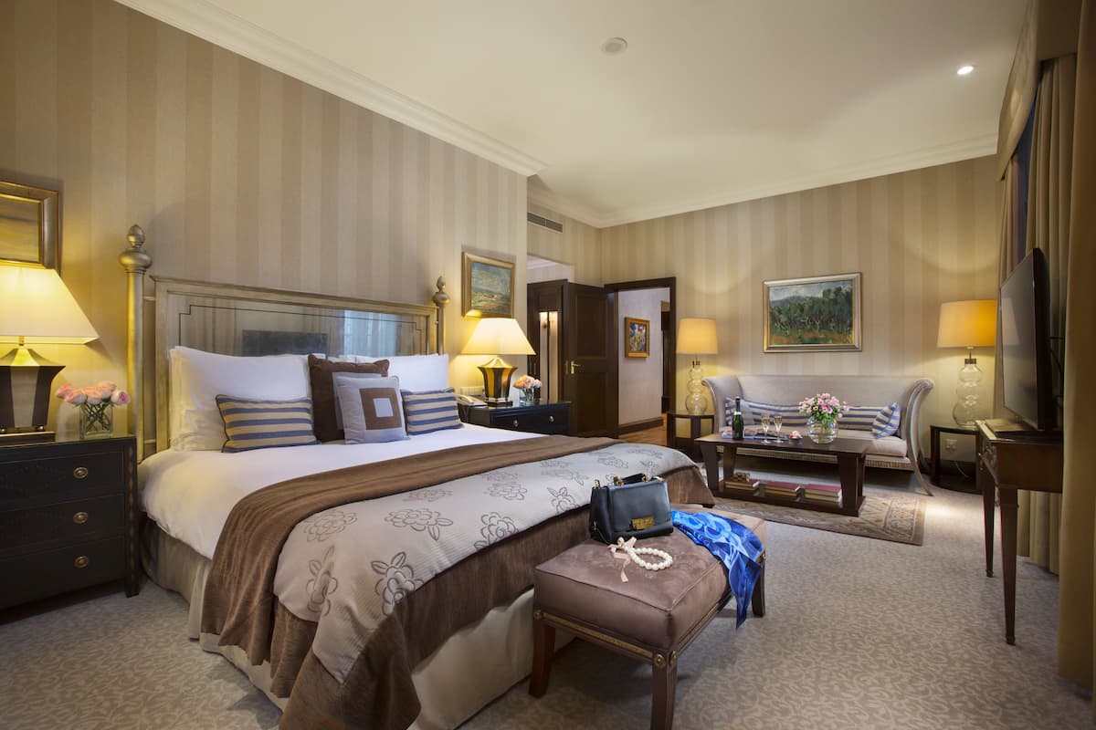 A hotel room with a large bed, a sitting area with a sofa and armchairs, a television, and a desk with a lamp.