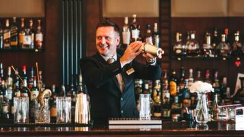 A bartender pouring a drink at a bar with shelves of liquor bottles in the background.