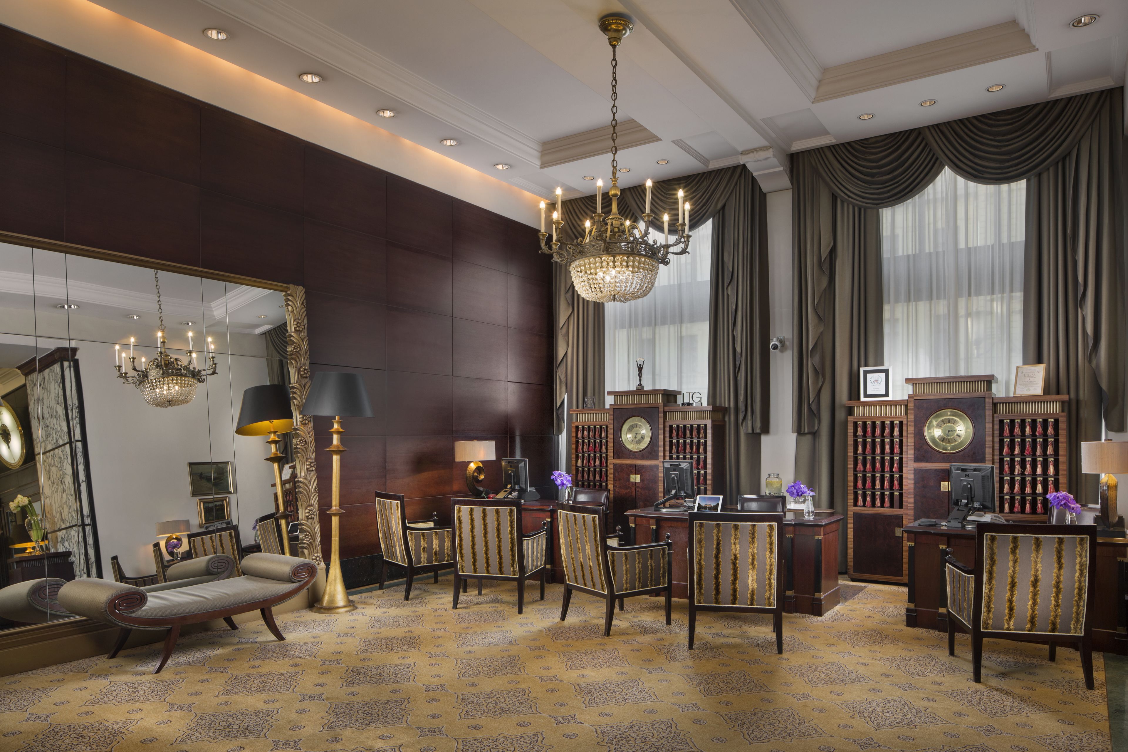 Une chambre luxueuse avec un grand miroir, des fauteuils élégants, un lustre et un bureau doté d’un téléphone et de livres.