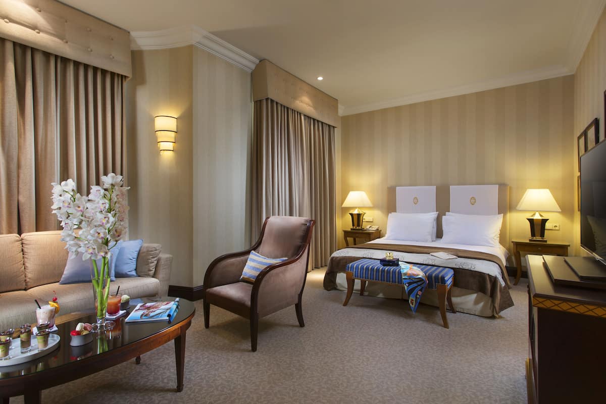 A hotel room with a bed, a sofa, a chair, a coffee table with drinks, and a TV.