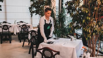 A restaurant with tables set for dining, a waiter attending to a table, and indoor plants.