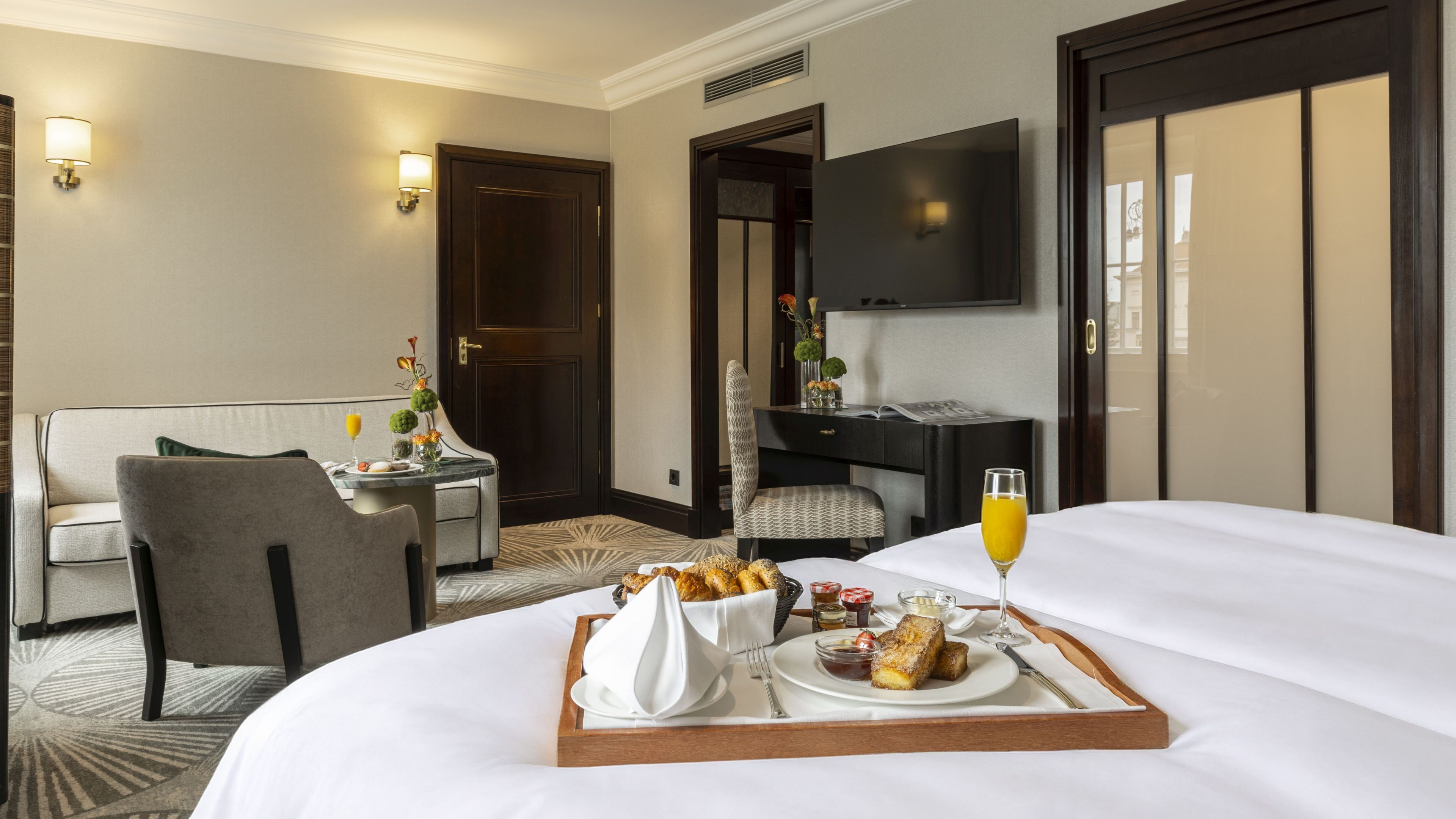 A hotel room with a bed, a dining table with breakfast, a TV, and a door.