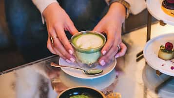 En person serverer en kop kaffe med latte-kunst i et glas.