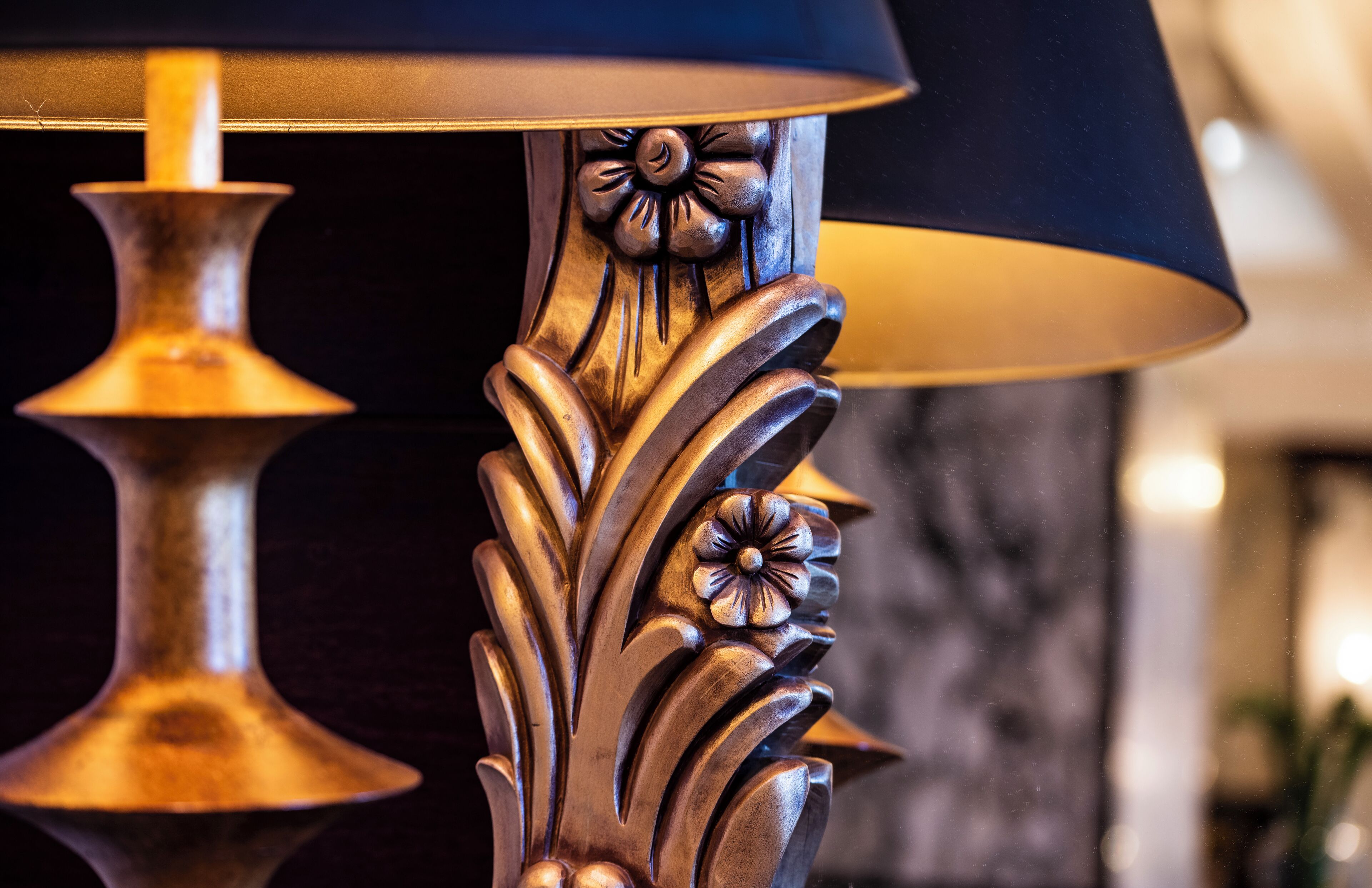 A close-up of a lamp with a dark shade and a decorative base with floral patterns.