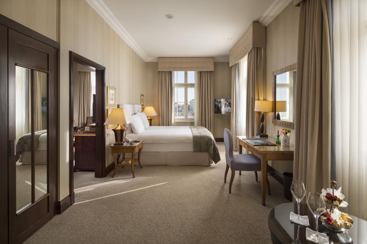 A hotel room with a bed, desk, chair, and a small table with a vase and flowers.