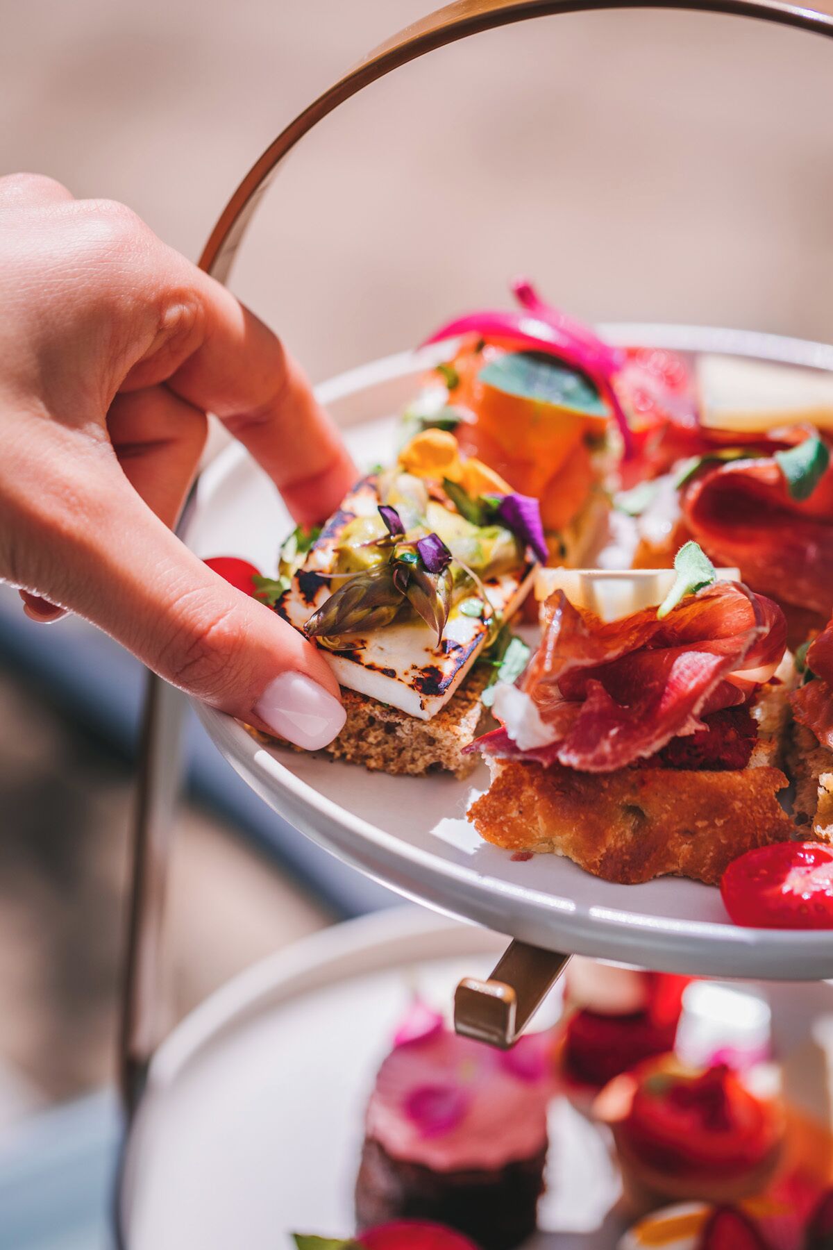 A hand holding a tray with various food items, including a piece of bread with cheese and greens, and a slice of meat.