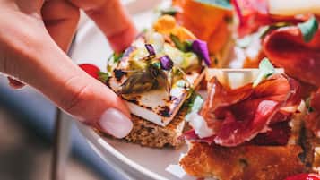 A hand holding a tray with various food items, including a piece of bread with cheese and greens, and a slice of meat.