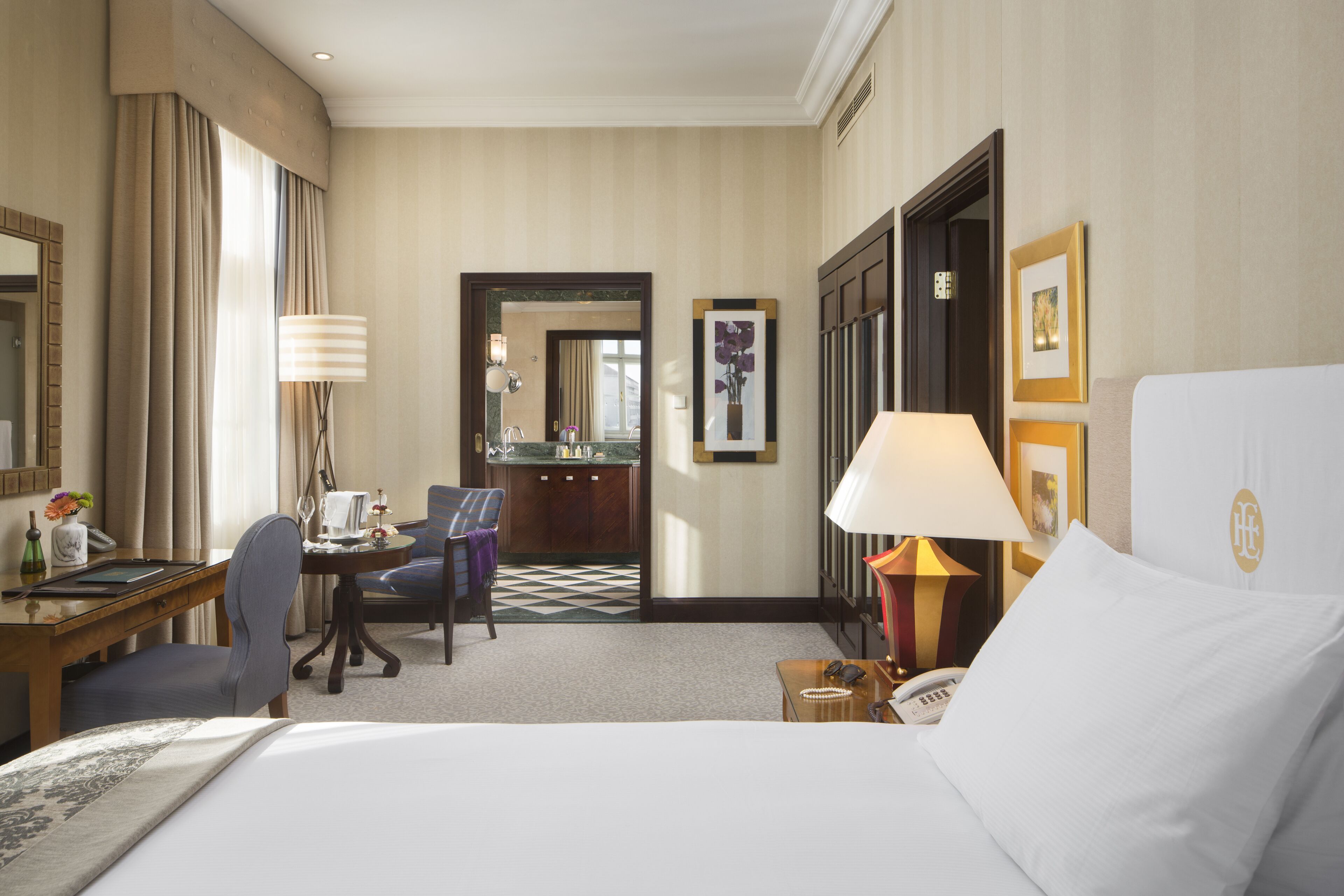A hotel room with a large bed, a desk with a chair, a desk lamp, a telephone, and a mirror.