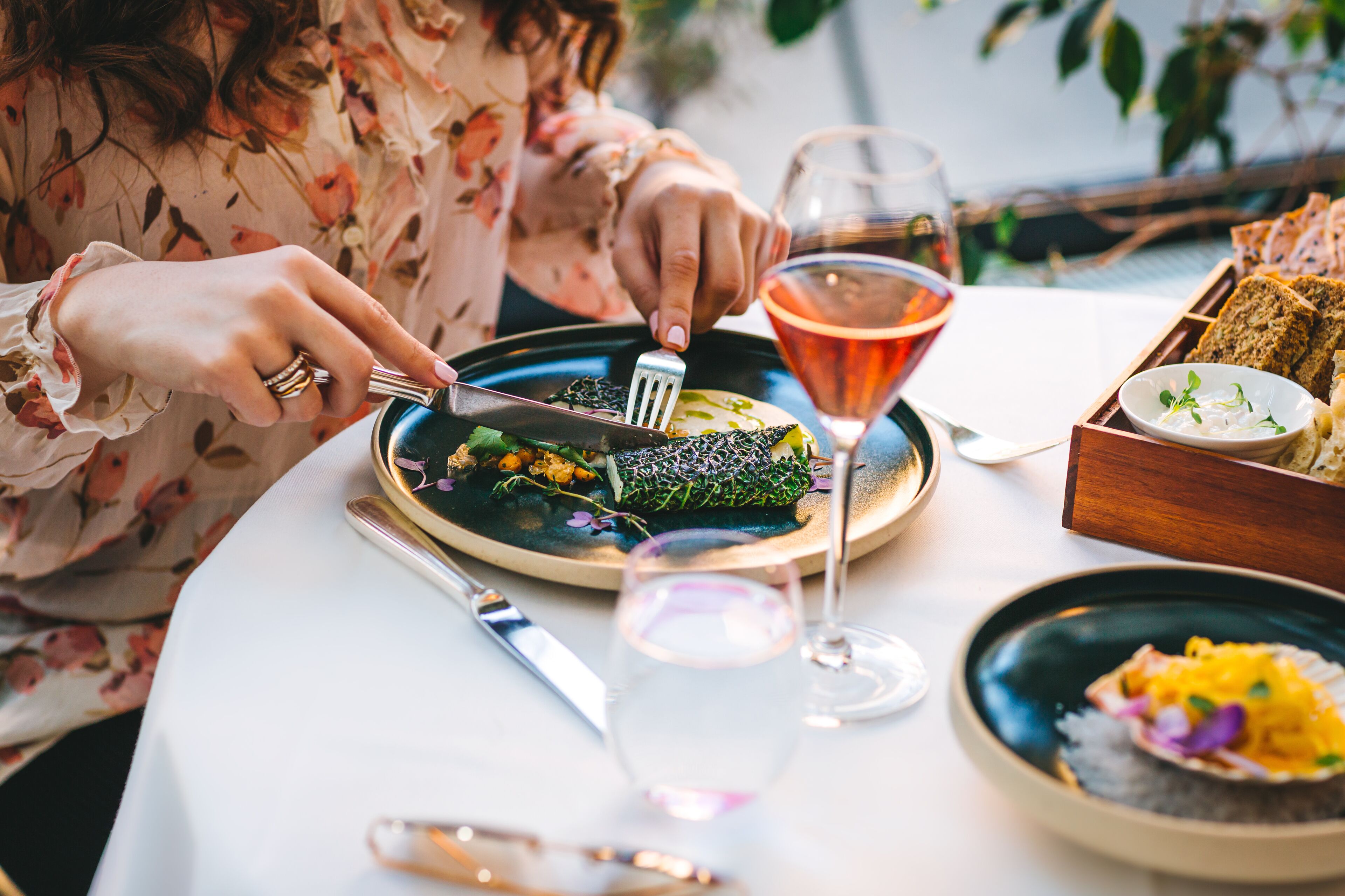 A dining table with a plate of food, a fork, a knife, a glass of wine, and a bowl of soup.