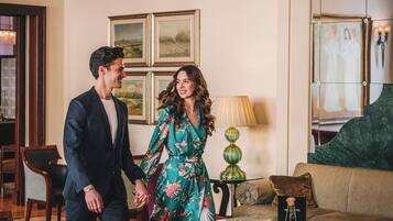 A couple holding hands in a well-lit room with a chandelier, framed artwork on the wall, and a sofa.