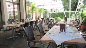 Un restaurant en plein air avec des chaises et des tables en osier, un présentoir à menus et, au fond, une enseigne pour Erdinger Weibling.