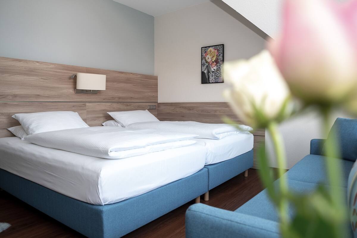 Quarto de hotel moderno com uma cama grande, mesa de cabeceira, cadeira e luminária fixada na parede.