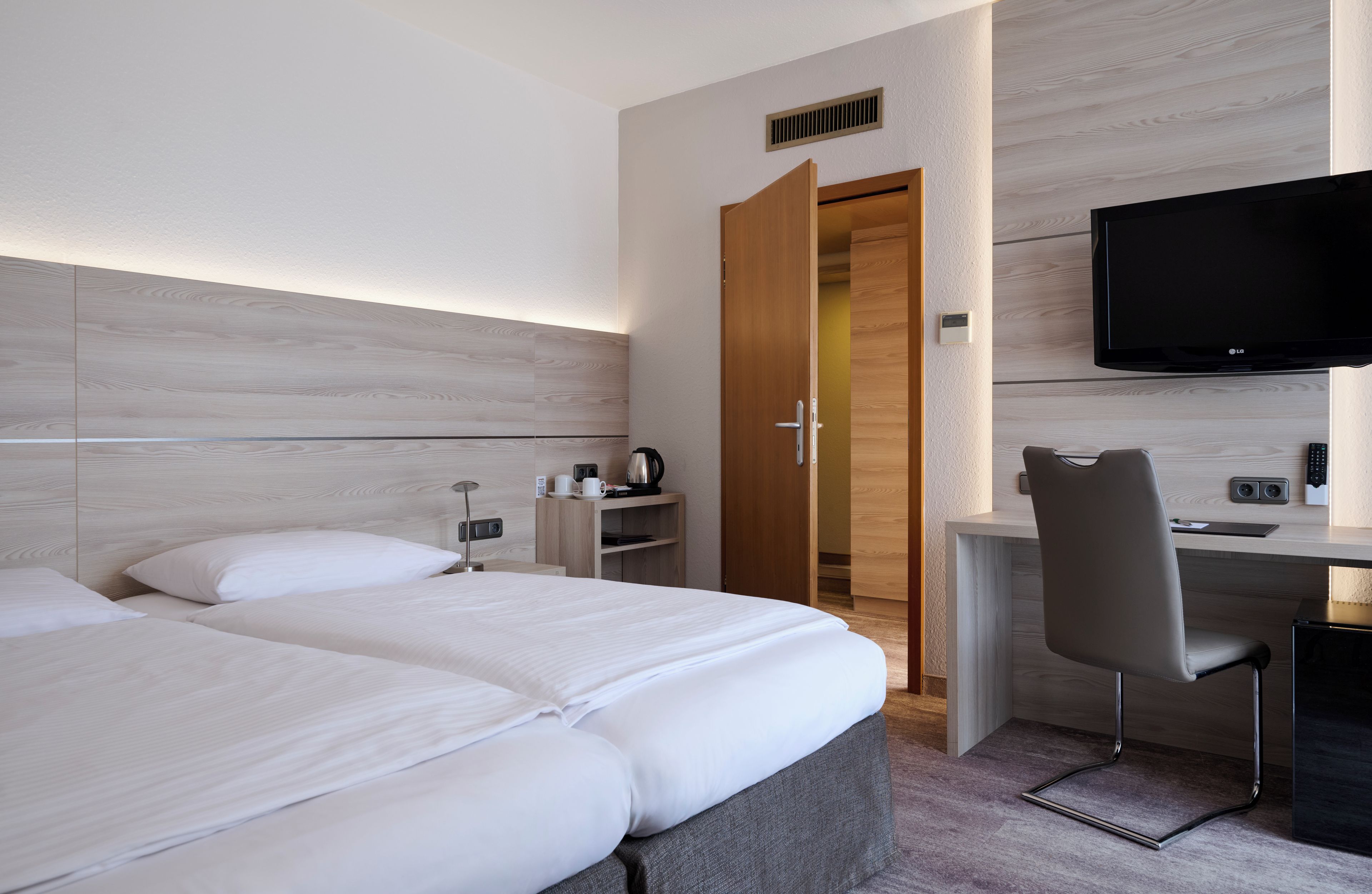 Ein Hotelzimmer mit Bett, Schreibtisch, Stuhl, Fernseher und Kleiderschrank.