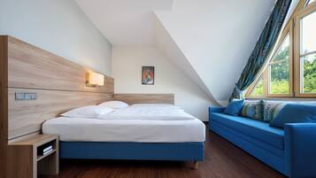 A bedroom with a bed, a blue sofa, a nightstand, a wall-mounted lamp, and a window with curtains.