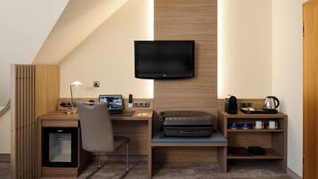 Une chambre d’hôtel de taille réduite, équipée d’un bureau, d’une chaise, d’une télévision et d’un petit coin cuisine.