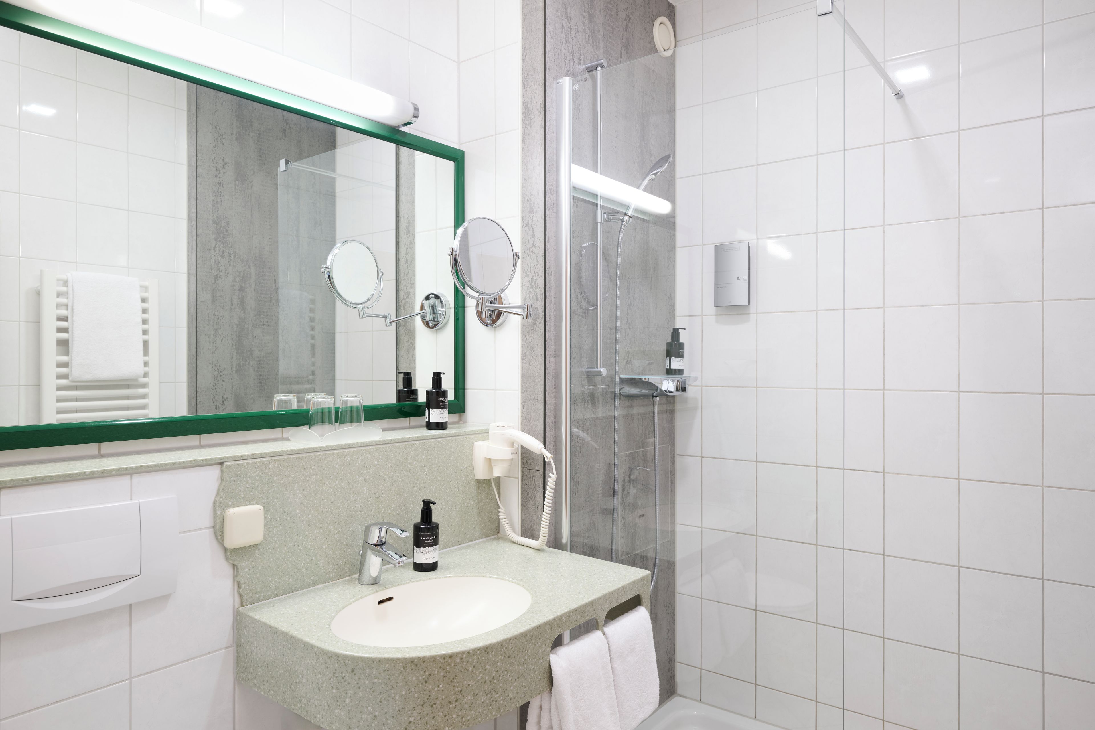 Een moderne badkamer met een granieten wastafel, een grote spiegel, een handdouche en een douche met glazen wanden.