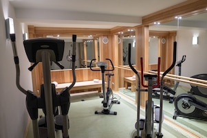 Un gimnasio con diferentes equipos de ejercicio, un espejo grande y un banco de madera.