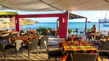 An outdoor dining area with tables and chairs, a view of the ocean, and a red archway with the word "Dodgy".