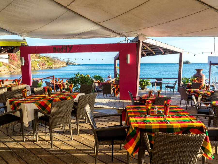 An outdoor dining area with tables and chairs, a view of the ocean, and a red archway with the word "Dodgy".