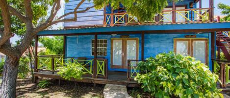Un bâtiment à deux étages, à la façade bleue, doté de balcons en bois et d’un petit jardin.