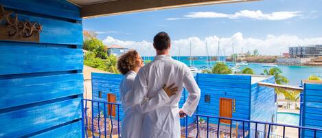 A couple embracing on a balcony overlooking a marina with boats and a clear sky.