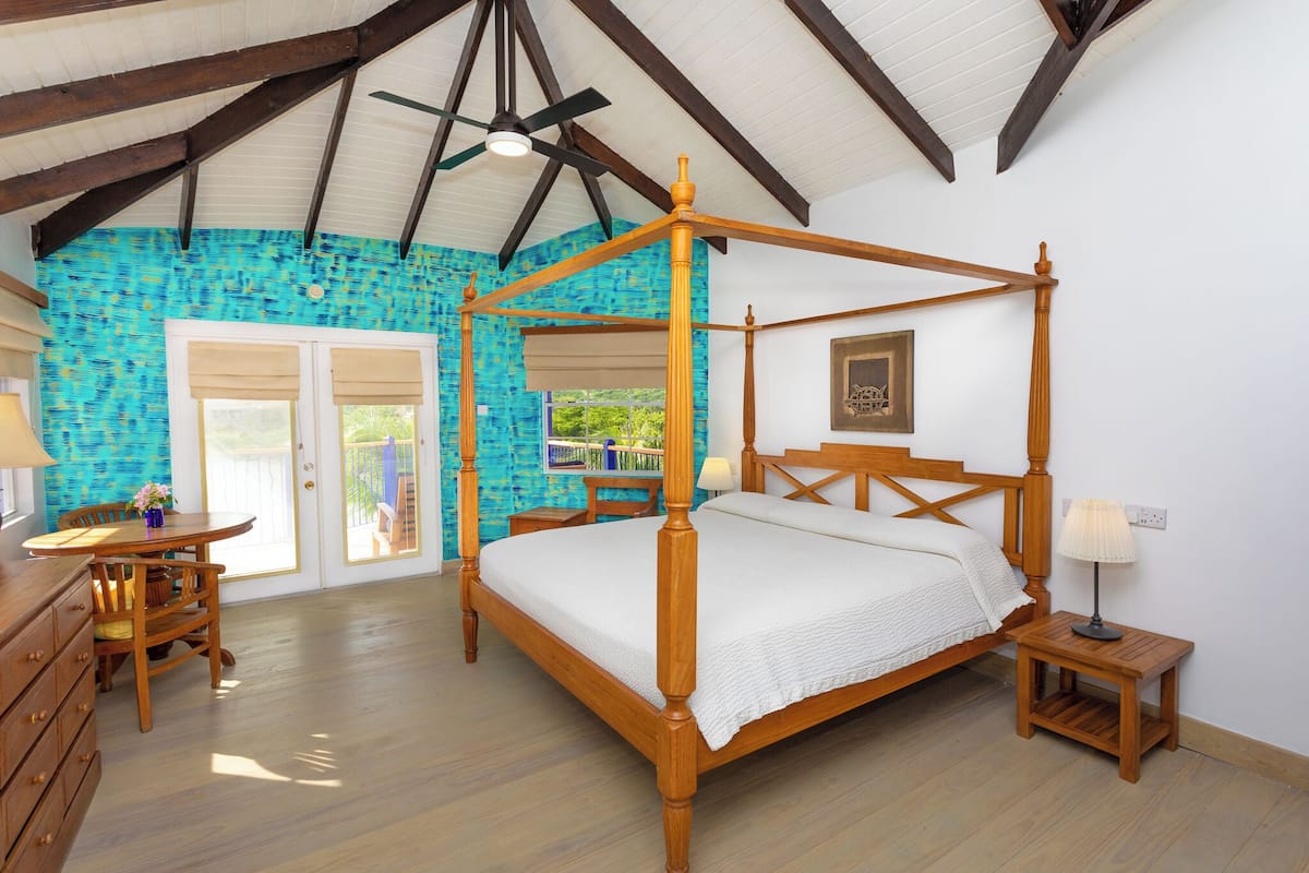 A spacious bedroom with a four-poster bed, wooden furniture, and a view through a glass door.