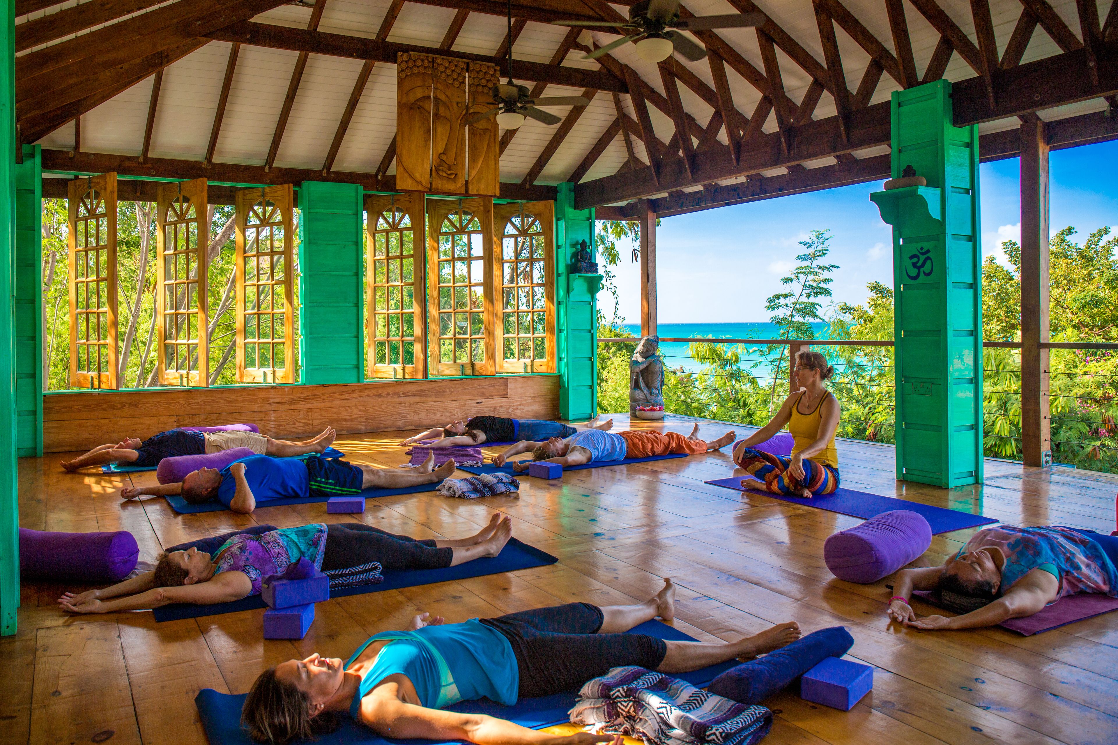 Clase de yoga en una sala de madera con ventanas amplias y vista al océano.