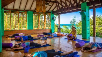Clase de yoga en una sala de madera con ventanas amplias y vista al océano.