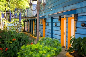 A row of blue and orange buildings with doors and windows, surrounded by greenery.