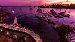 A marina with multiple boats docked, a wooden pier, and a sunset in the background.