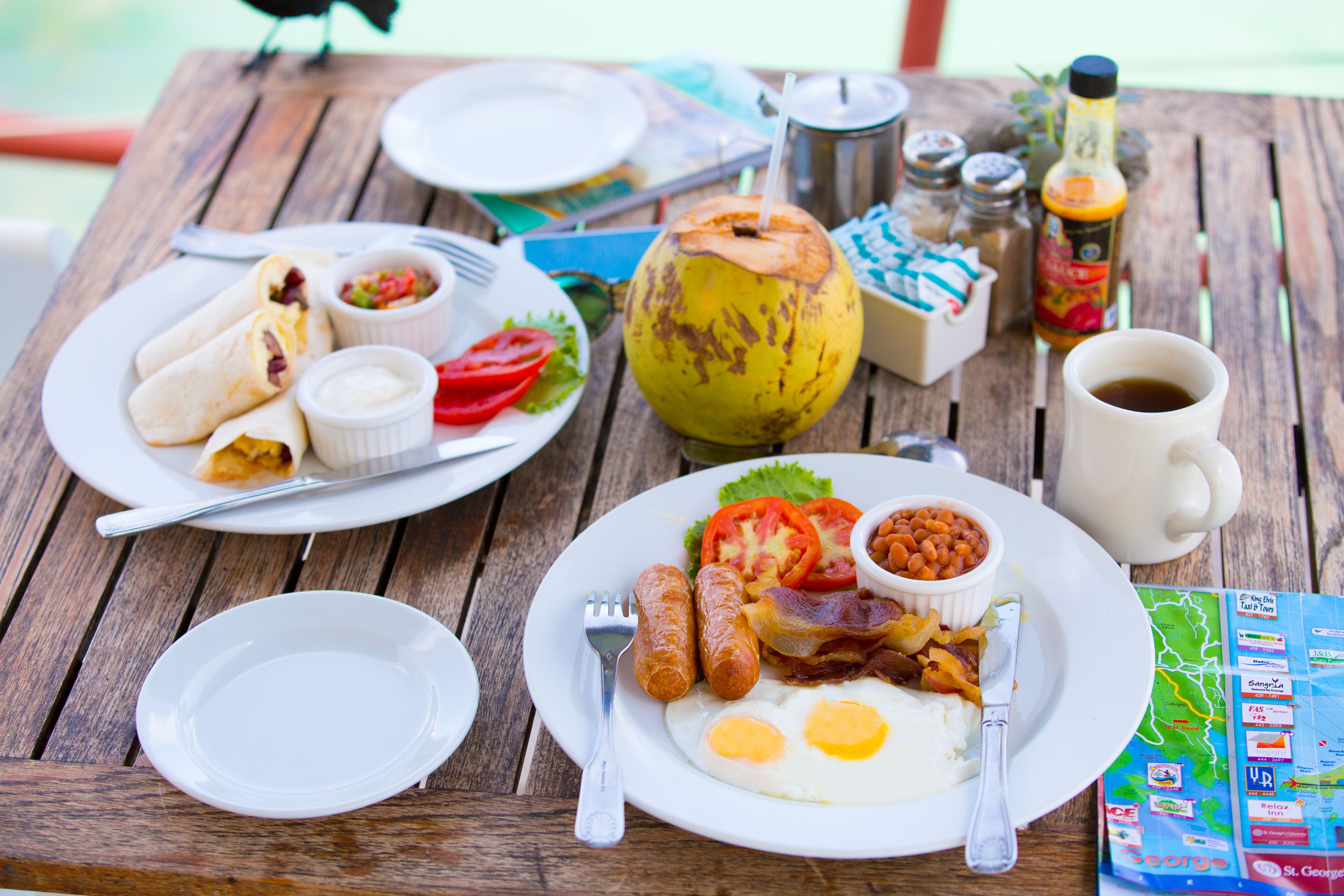 A wooden table with breakfast items including eggs, sausages, and a coconut.