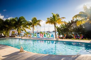 Una piscina con un cartel que dice "Grenada", rodeada de palmeras y sillas de descanso.