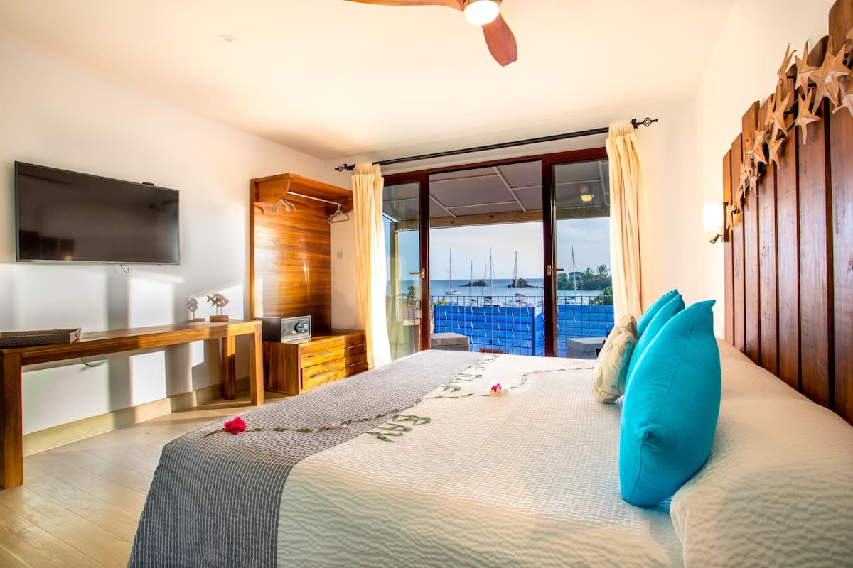A bedroom with a bed, a TV, a desk, and a view of the sea.