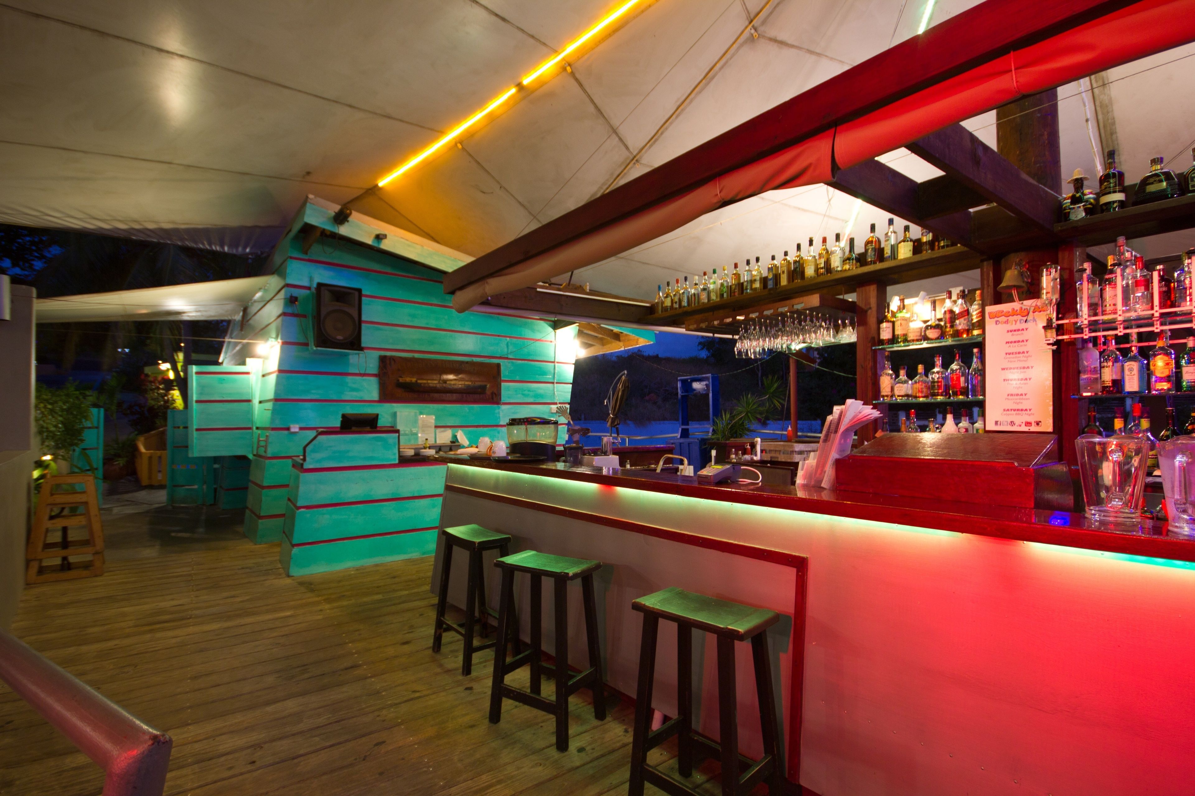 A bar area with a wooden floor, bar stools, and shelves of bottles.
