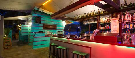 A bar area with a wooden floor, bar stools, and shelves of bottles.